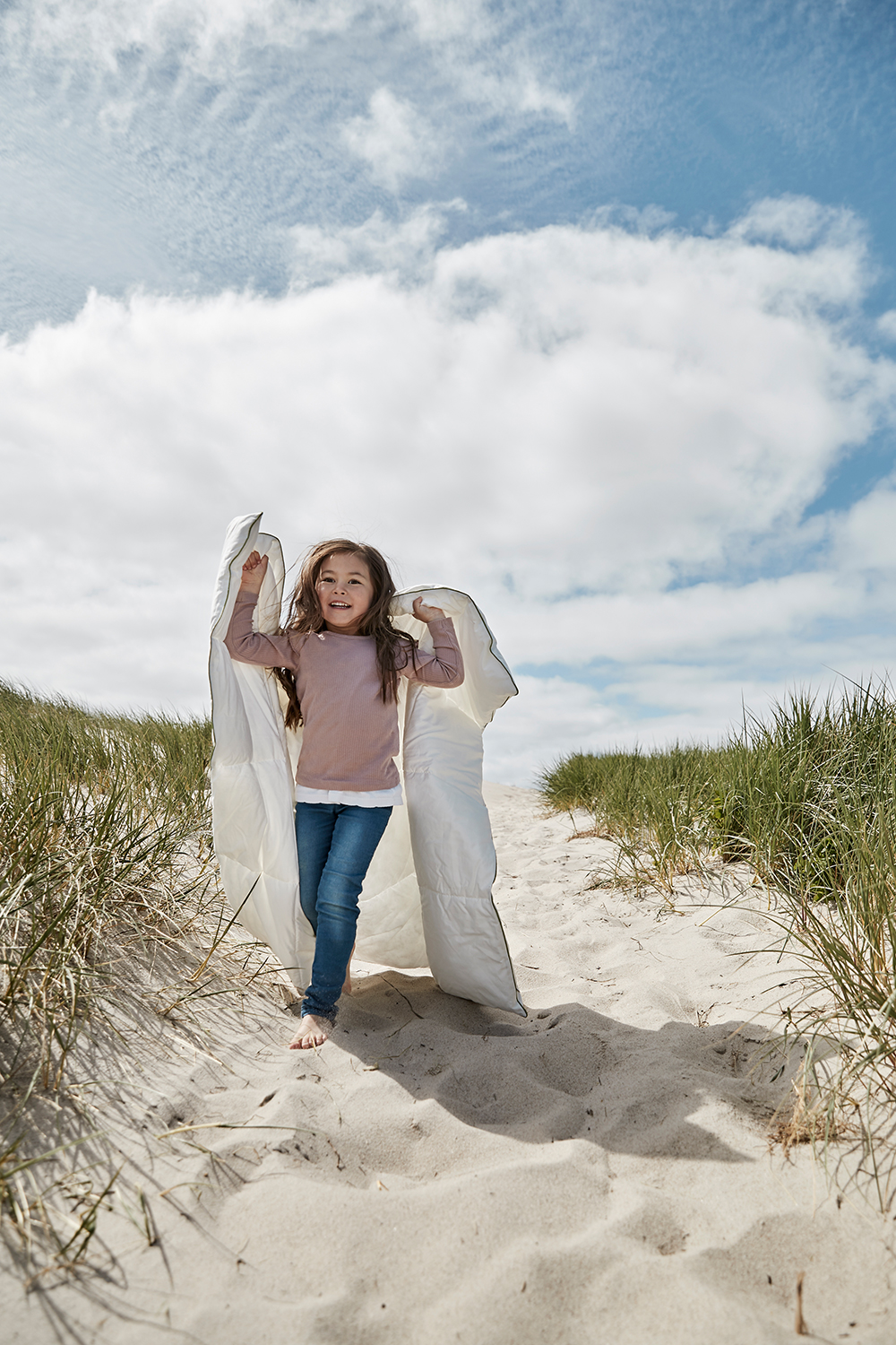 Et barn bærer en hvid dyne på en sti ved stranden